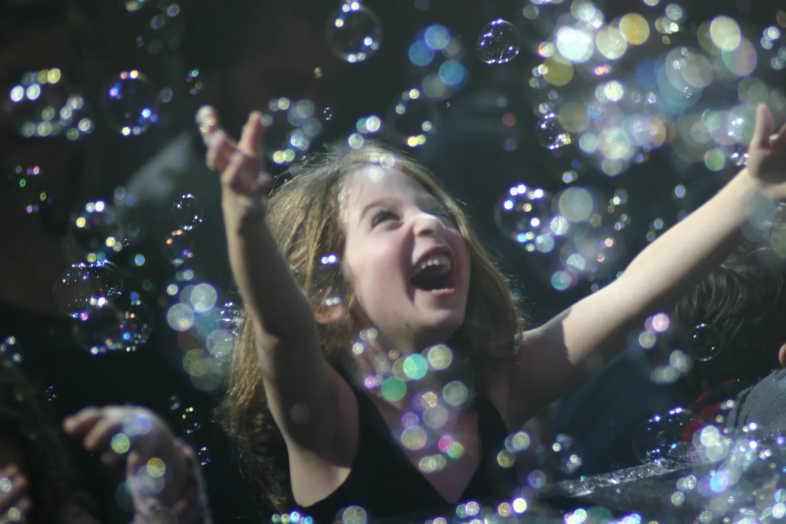 A delighted girl reaching for bubbles in the audience