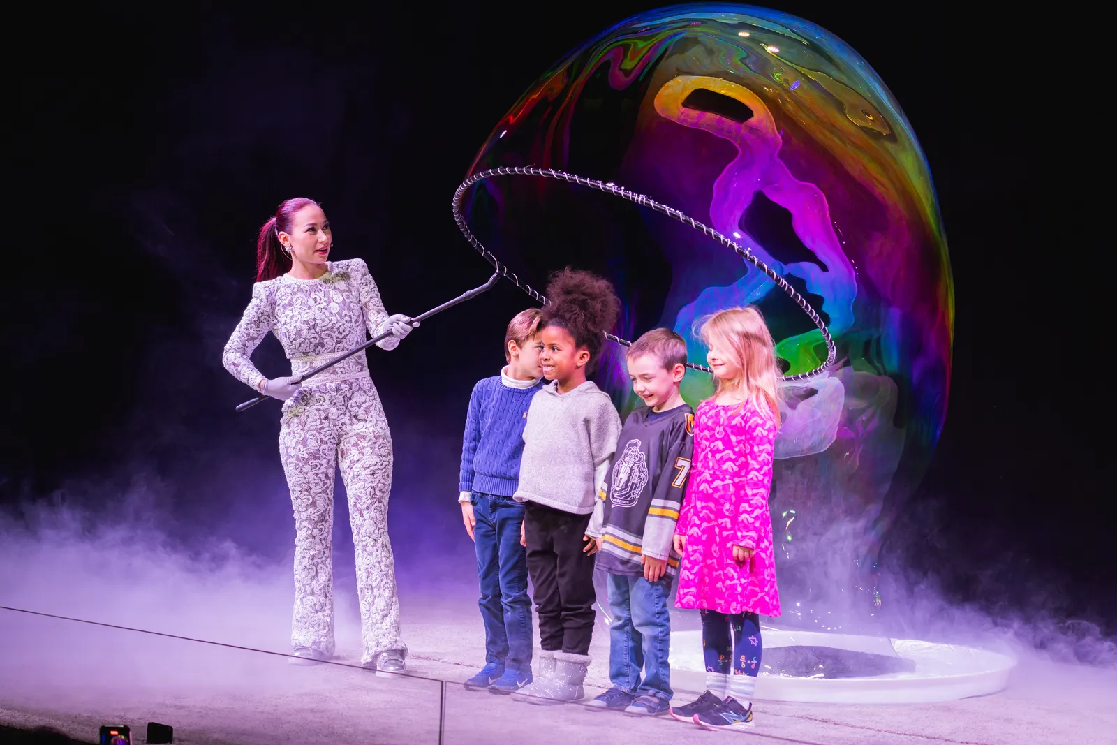 Children from the audience on stage beside a giant rainbow bubble