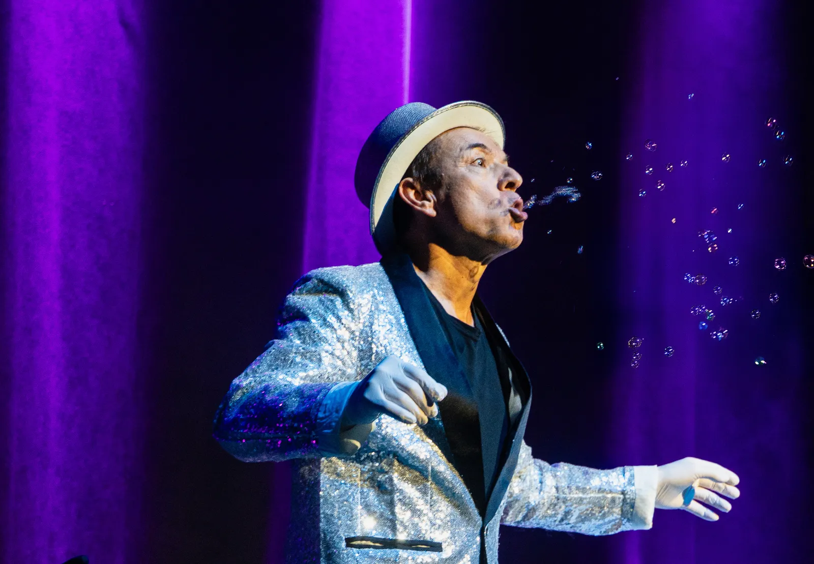A bubble artist in a sequin jacket blowing a stream of bubbles